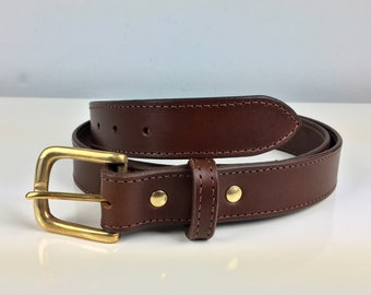May include: A brown leather belt with a brass buckle. The belt has a stitched edge and a pointed tip.