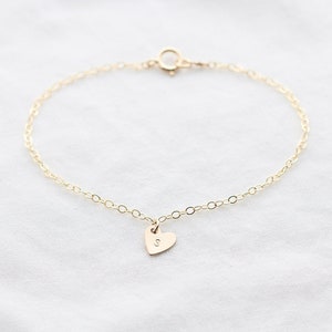 Puede incluir: Un brazalete de cadena dorada con un pequeño dije en forma de corazón grabado con la letra "S".