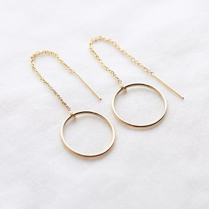 May include: A pair of gold hoop earrings with a delicate chain dangling from each hoop.