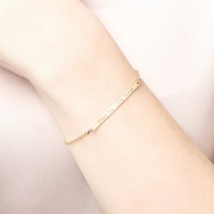 Op de afbeelding: Een gouden armband met een staaf en een delicate ketting. De staaf heeft de inscriptie "Enjoy the little things".