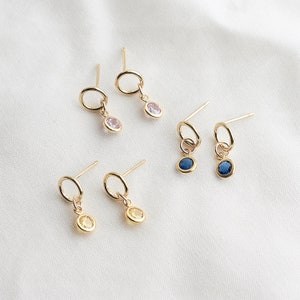 May include: A set of six gold earrings with small round gemstones. The earrings feature a simple circle design with a dangling gemstone. The gemstones are pink, blue, and yellow.