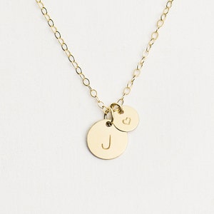May include: Gold necklace with a small heart charm and a larger charm with the letter J engraved on it.