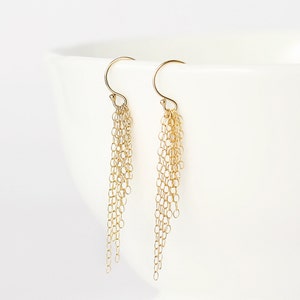 May include: A pair of gold dangle earrings with multiple chains hanging from the bottom. The chains are made of small, linked circles.