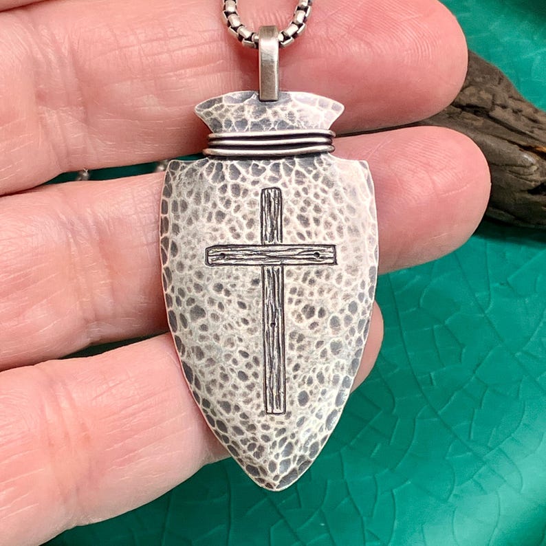 Peut inclure: Un collier pendentif argent&eacute; avec un motif de pointe de fl&egrave;che et une surface textur&eacute;e. Le pendentif pr&eacute;sente une croix grav&eacute;e au centre. Le collier est sur une cha&icirc;ne argent&eacute;e.
