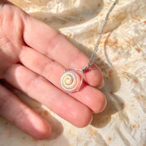 May include: A silver chain necklace with a pink and yellow iridescent shell pendant. The shell has a spiral pattern.
