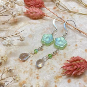 May include: A pair of silver dangle earrings with green flower-shaped glass beads and clear teardrop-shaped glass beads.