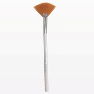 Op de afbeelding: Een witte make-upborstel met een waaiervormige kop van bruine haren. De steel heeft de tekst "Skin Beauty Solutions" erop gedrukt.