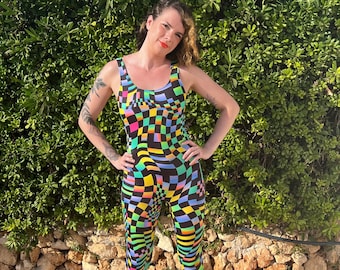 May include: A woman wearing a black and white checkered jumpsuit with colorful geometric patterns. The jumpsuit has a scoop neck and sleeveless design.