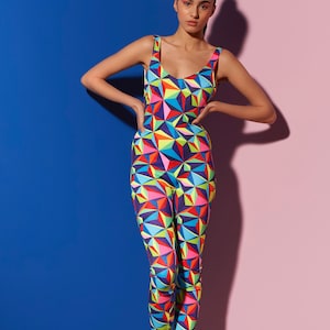 May include: A woman wearing a colourful geometric print jumpsuit with a scoop neck and sleeveless design. The jumpsuit is made of a stretchy fabric and has a fitted silhouette.