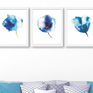May include: Three framed watercolor paintings of blue flowers with white accents. The flowers are painted in a loose, abstract style.