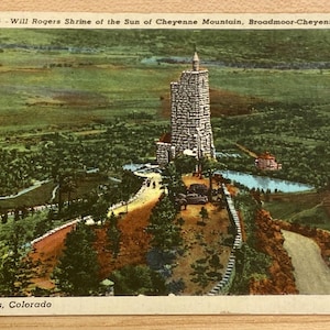 May include: A vintage postcard depicting the Will Rogers Shrine of the Sun, a stone building on Cheyenne Mountain in Colorado Springs, Colorado. The postcard features a scenic aerial view of the building and surrounding landscape.