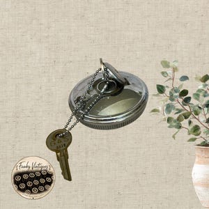 May include: A circular, silver-toned metal gas cap featuring a locking mechanism with a keyhole. A metal ball chain is attached to the cap, connecting to a brass-colored key with the word GAS and the number 4878 embossed on its surface.