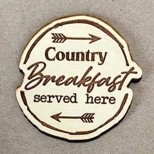 May include: A wooden sign with the words "Country Breakfast served here" in a rustic font. The sign is circular with a light-colored center and a dark brown border. Arrows point towards the text.