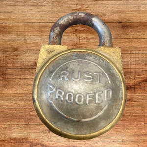 May include: A brass padlock with a round, silver-colored face that reads "RUST PROOFED".