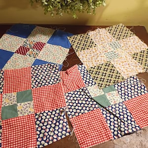 May include: Four colorful patchwork quilt squares in various stages of completion. The squares feature a mix of floral, gingham, and polka dot patterns in red, blue, green, and white. The unfinished edges show loose threads.