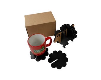 May include: A red mug with the "LYONS" logo, a brown cardboard box, two black flower-shaped coasters, and a black sheep-shaped decoration. The mug sits on a black coaster. The sheep decoration is made of layered wood.