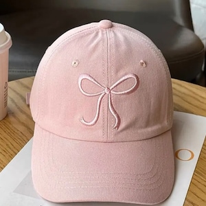 Peut inclure: Une casquette de baseball rose avec un nœud rose brodé sur le devant.