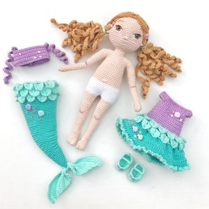 May include: A crocheted mermaid doll with long brown hair, a white swimsuit, and a turquoise and purple mermaid tail. The doll is wearing a purple and turquoise dress with a scalloped edge.