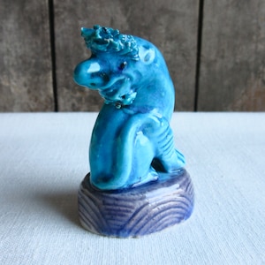 May include: A blue ceramic figurine of a mythical creature with a crown, sitting on a blue and white base.