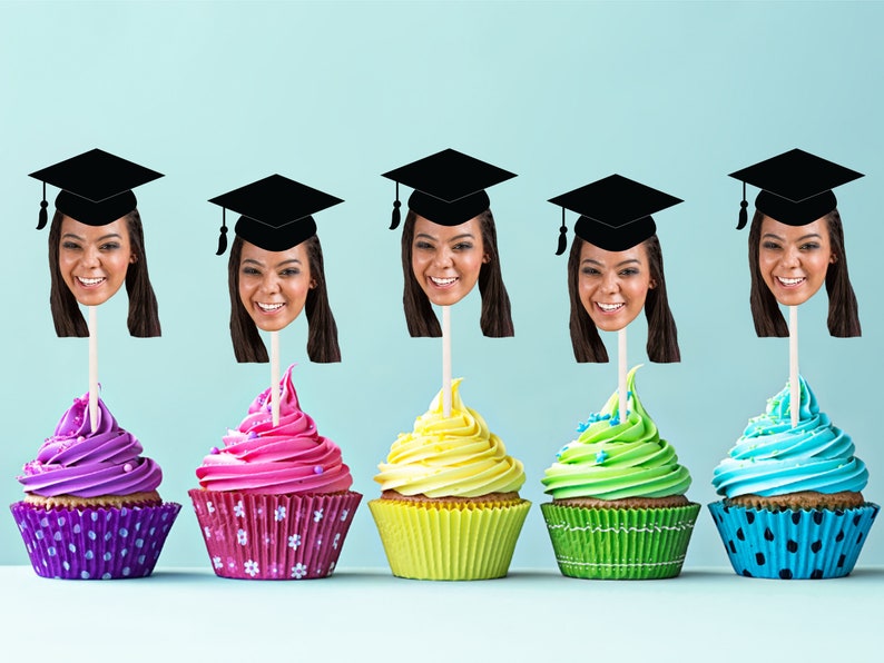 May include: Five cupcakes decorated with colorful frosting and topped with graduation caps and faces. The cupcakes are arranged in a row on a light blue background.