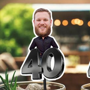 May include: A black and white cake topper featuring a caricature of a person with a beard and the number 40. The person is wearing a black shirt and is standing in front of the number 40.
