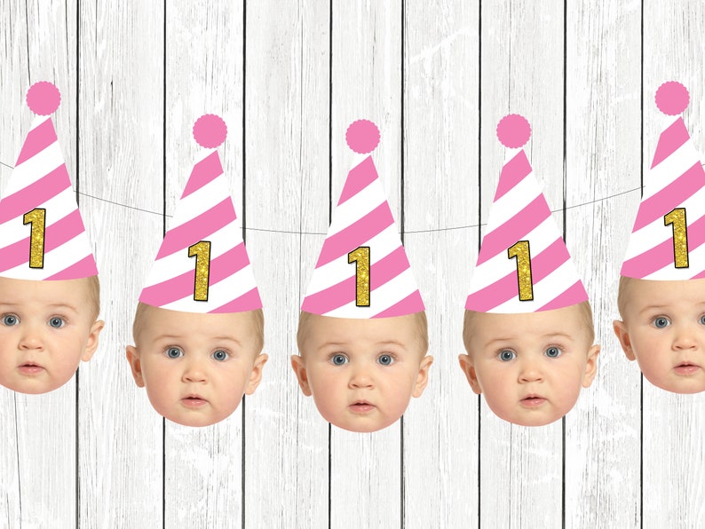 Op de afbeelding: Een roze-wit gestreepte feestbanner met vijf babygezichten die roze-witte feestmutsen dragen met gouden glitter "1"s.