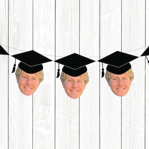 May include: A graduation banner with five black graduation caps and faces of a person wearing each cap. The banner is strung on a white wooden background.