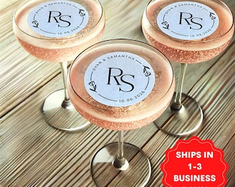 May include: Three champagne flutes with personalized round stickers. Each sticker features a white background with a black circle containing the initials "RS" and the date "10.06.2026". The stickers are decorated with small floral designs.