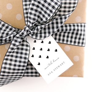 May include: A brown gift box with white polka dots wrapped with a black and white gingham ribbon. A white gift tag with black hearts and the text "with love Ava Stewart" is attached to the box.