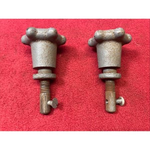 May include: Two vintage metal knobs with a flower-like top design. The knobs have a threaded shaft and a small screw. The metal has a worn, aged appearance. The background is a solid red color.