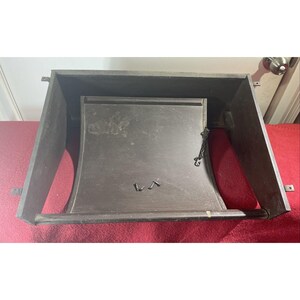 May include: A dark brown wooden wall-mounted shelf with a curved front and a metal chain hanging from the top. The shelf has a wooden rod across the front and two small metal hooks on the bottom.