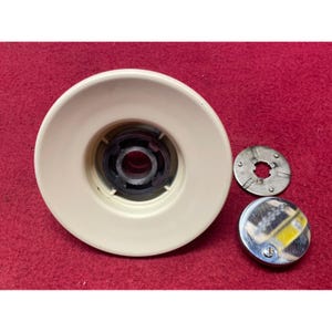 May include: An off-white, circular component with a central black core, accompanied by a small, silver metal disc and a chrome-finished cap. The items are arranged on a red surface, suggesting a mechanical or industrial theme.