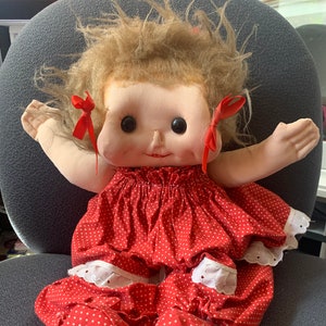 May include: A handmade doll with a red and white polka dot dress and matching shoes. The doll has brown hair, brown eyes, and a smiling face.