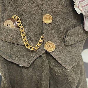 May include: Close-up of a dark gray vest with gold-colored buttons and a pocket watch. The watch is in a pocket with a gold chain attached to the vest. The vest has a textured appearance.
