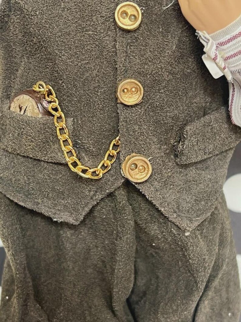 May include: Close-up of a dark gray vest with gold-colored buttons and a pocket watch. The watch is in a pocket with a gold chain attached to the vest. The vest has a textured appearance.