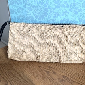 May include: A woven straw clutch with a black strap. The clutch has a rectangular shape and a woven pattern.