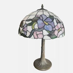 May include: A stained glass table lamp with a floral design in shades of purple, pink, and green. The lamp has a bronze base with a tree-like design.