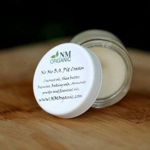 May include: A white jar with a white lid labeled "No Mo B.O. Pit Cream" with the ingredients listed below. The jar is open and the cream inside is white.