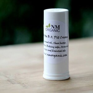 May include: White deodorant stick with a label that reads "NM ORGANIC Mo B.0. Pit Cream Coconut oil, Shea butter, Baking soda, Arrowroot powder and Essential oils. www.nmorganic.com"