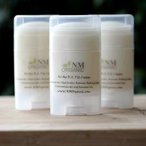May include: Three white plastic deodorant containers with a green leaf logo and the text "NM ORGANIC" and "No Mo B.O. Pit Cream". The text below the logo reads "Coconut oil, Shea butter,  Beeswax, Baking soda, Arrowroot powder and Essential oils. www.NMOrganic.com"