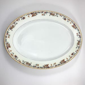 Puede incluir: Plato ovalado blanco para servir con borde dorado y un diseño floral en tonos marrones, verdes y rojos.