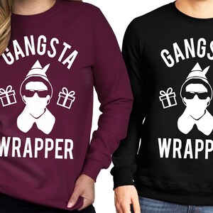 Könnte beinhalten: Zwei langärmelige Sweatshirts mit einer weißen Grafik einer Person, die einen Weihnachtsmann-Hut und eine Sonnenbrille trägt, mit dem Text "Gangsta Wrapper". Das Sweatshirt links ist weinrot und das Sweatshirt rechts ist schwarz.