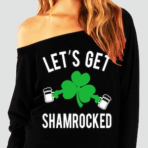 May include: Black off-the-shoulder sweatshirt with white text that reads "Let's Get Shamrocked" and a green shamrock with two beer mugs on either side.