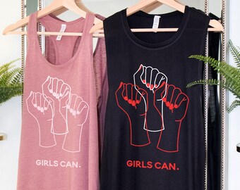 May include: Two sleeveless tops with a graphic of three raised fists and the text "GIRLS CAN." One top is black and the other is a dusty rose colour.
