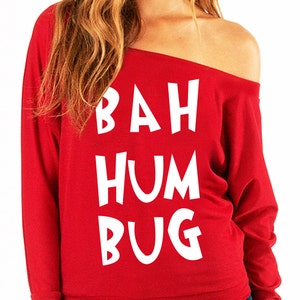Puede incluir: Camiseta roja de manga larga con hombros descubiertos y texto blanco que dice "BAH HUMBUG".