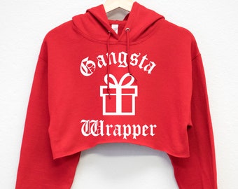 Pode incluir: Moletom vermelho com capuz cropped com uma estampa gráfica branca que diz "Gangsta Wrapper" em fonte inglesa antiga com uma ilustração de caixa de presente branca.