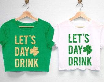 May include: Two cropped t-shirts with the text "Let's Day Drink" and a shamrock design in gold glitter. The shirts are green and white.