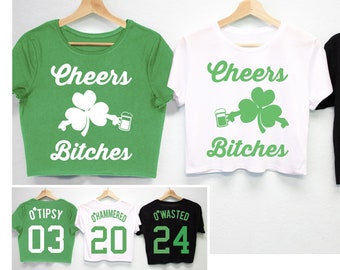 May include: Three cropped t-shirts with the text "Cheers Bitches" and a shamrock and beer mug graphic. The shirts are green, white, and black. Three additional t-shirts with the text "O'Tipsy 03", "O'Hammered 20", and "O'Wasted 24" are shown below.