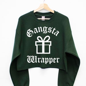 Könnte beinhalten: Ein dunkelgrüner, kurzer Pullover mit weißem Text, der "Gangsta Wrapper" lautet, und einer weißen Illustration einer Geschenkbox mit Schleife.