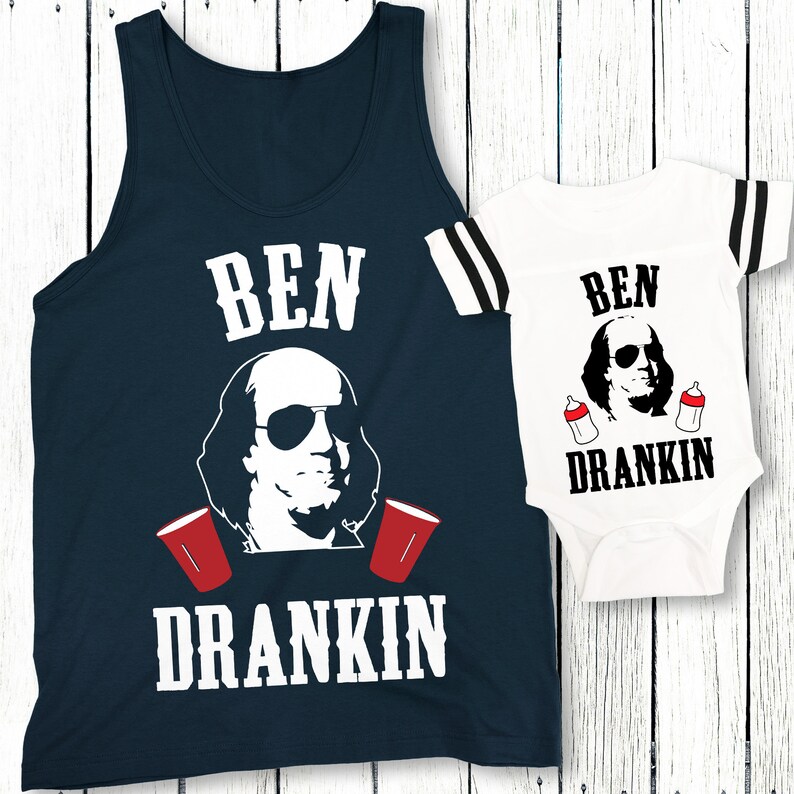 Op de afbeelding: Een marineblauw tanktop en een wit bodysuit met de tekst "BEN DRANKIN" en een cartoonafbeelding van Benjamin Franklin met een zonnebril. Het bodysuit heeft twee babyflesjes in plaats van rode bekers.